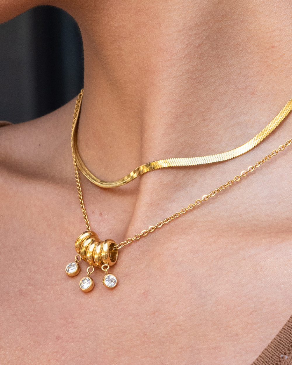 Gold necklace with a pendant on a person's neck against a neutral background
