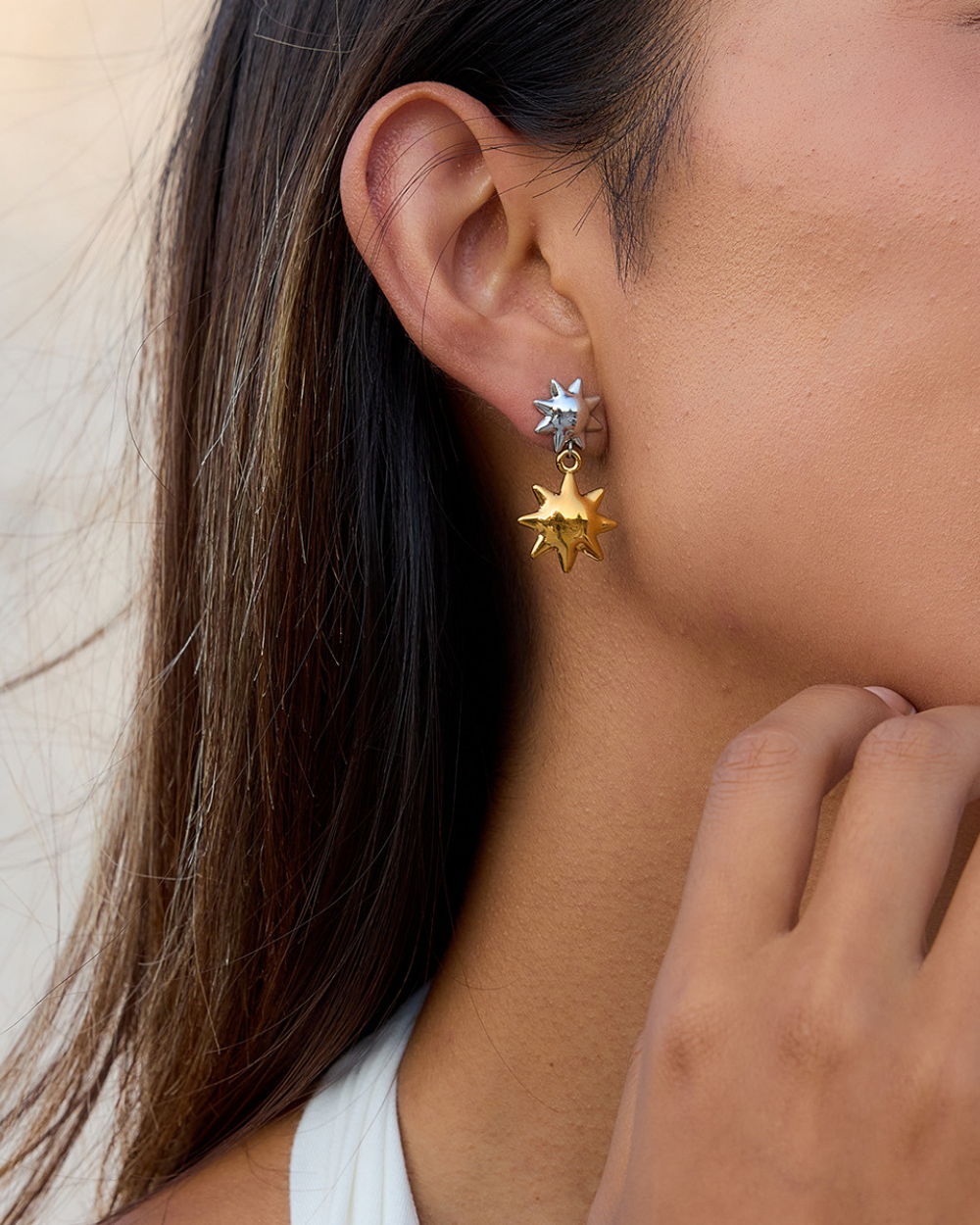 Close-up of a person wearing gold star-shaped earrings with a neutral background