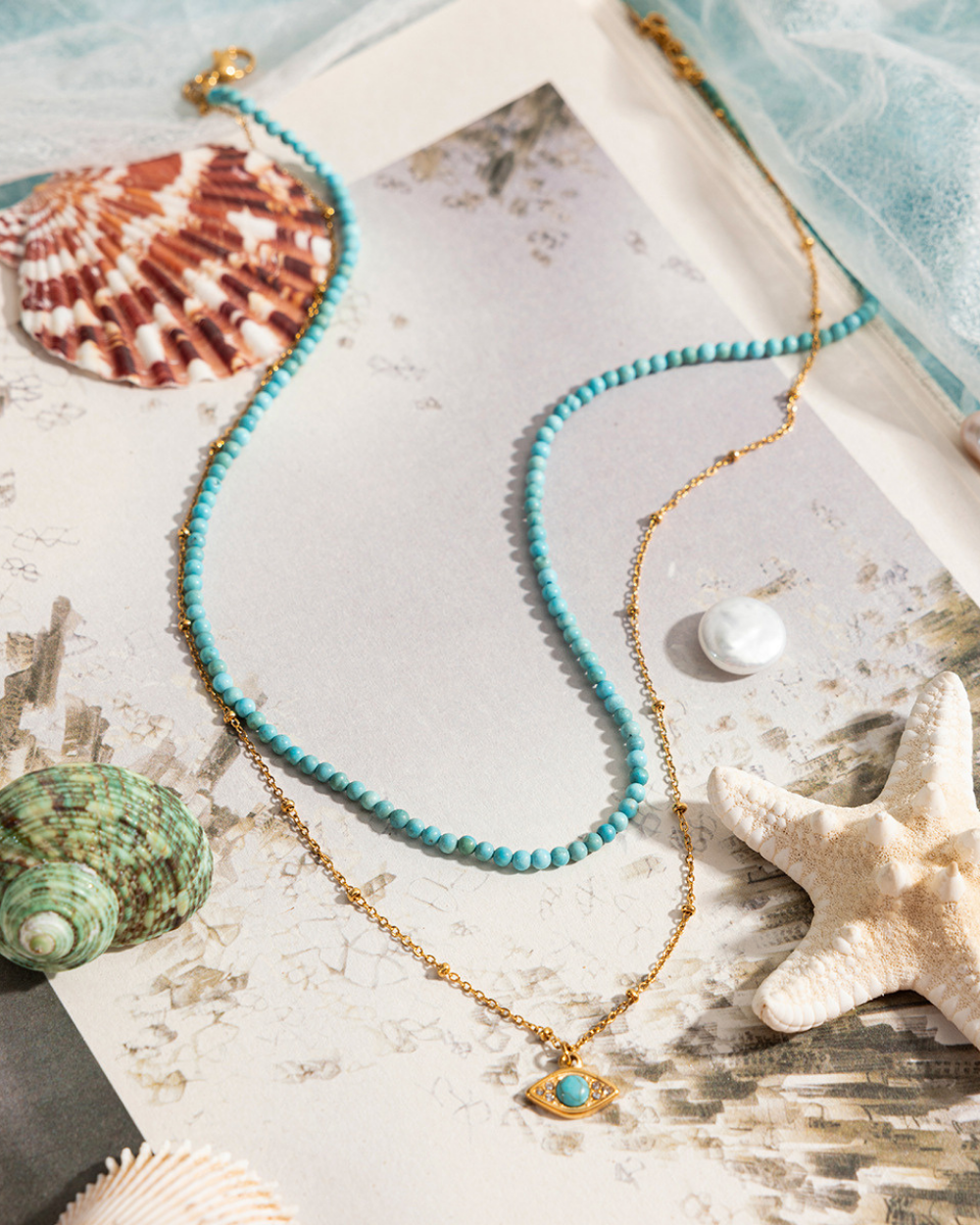 Turquoise beaded necklace with gold chain on a textured surface with shells and starfish.
