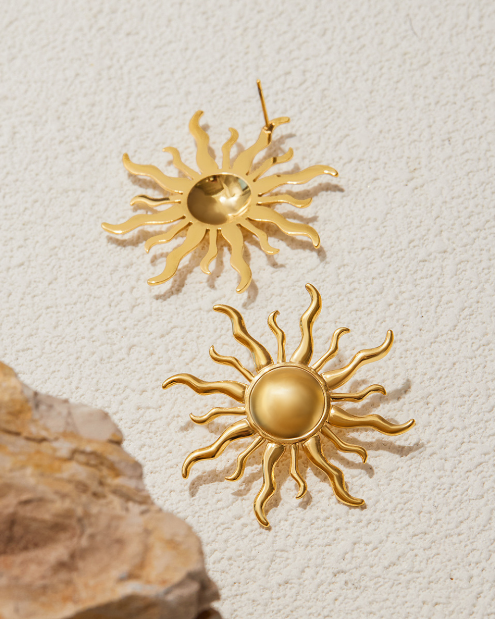 Gold sun-shaped earrings on a textured beige background