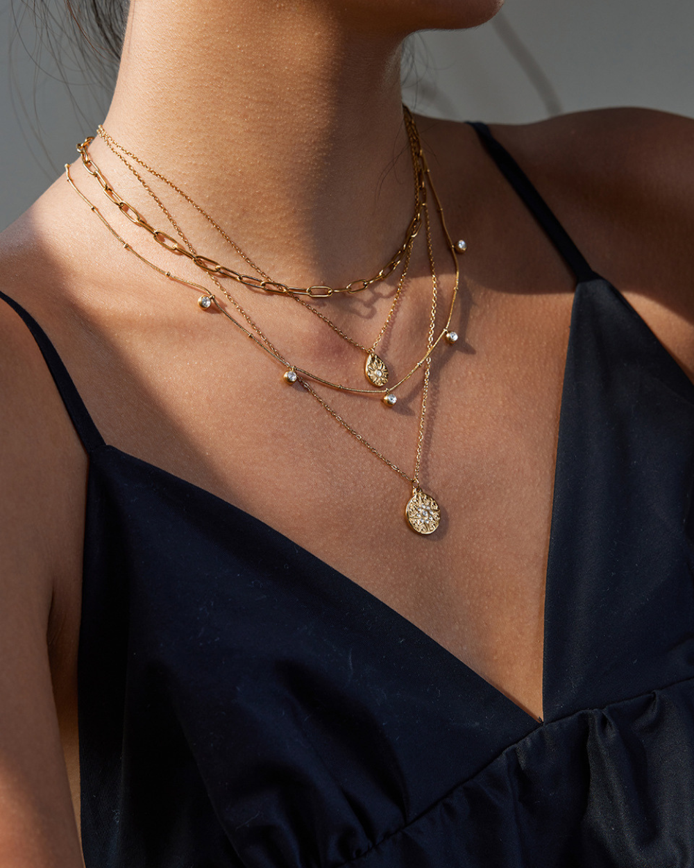 Close-up of a person wearing multiple gold necklaces with a black top.
