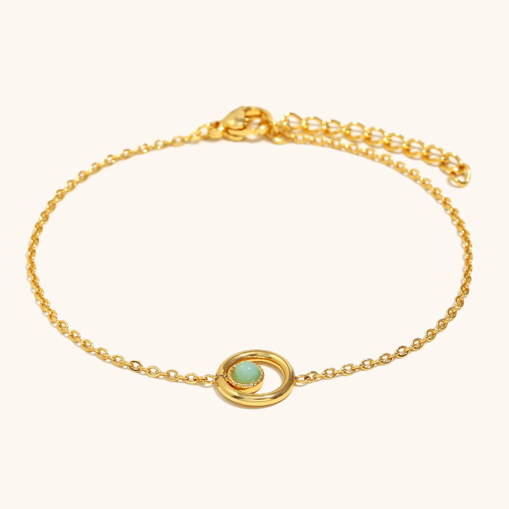 Delicate gold chain bracelet with green gemstone center and orbit-style design.