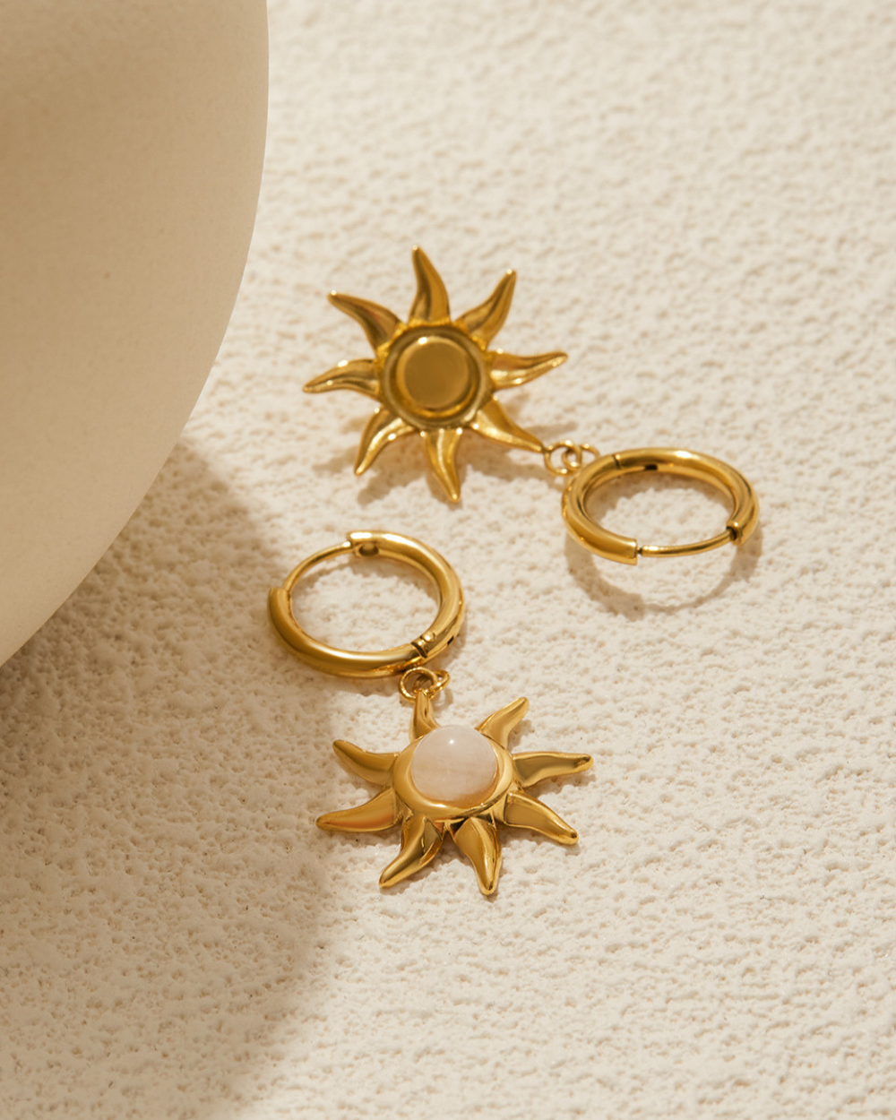 Gold sun-shaped earrings on a textured beige surface