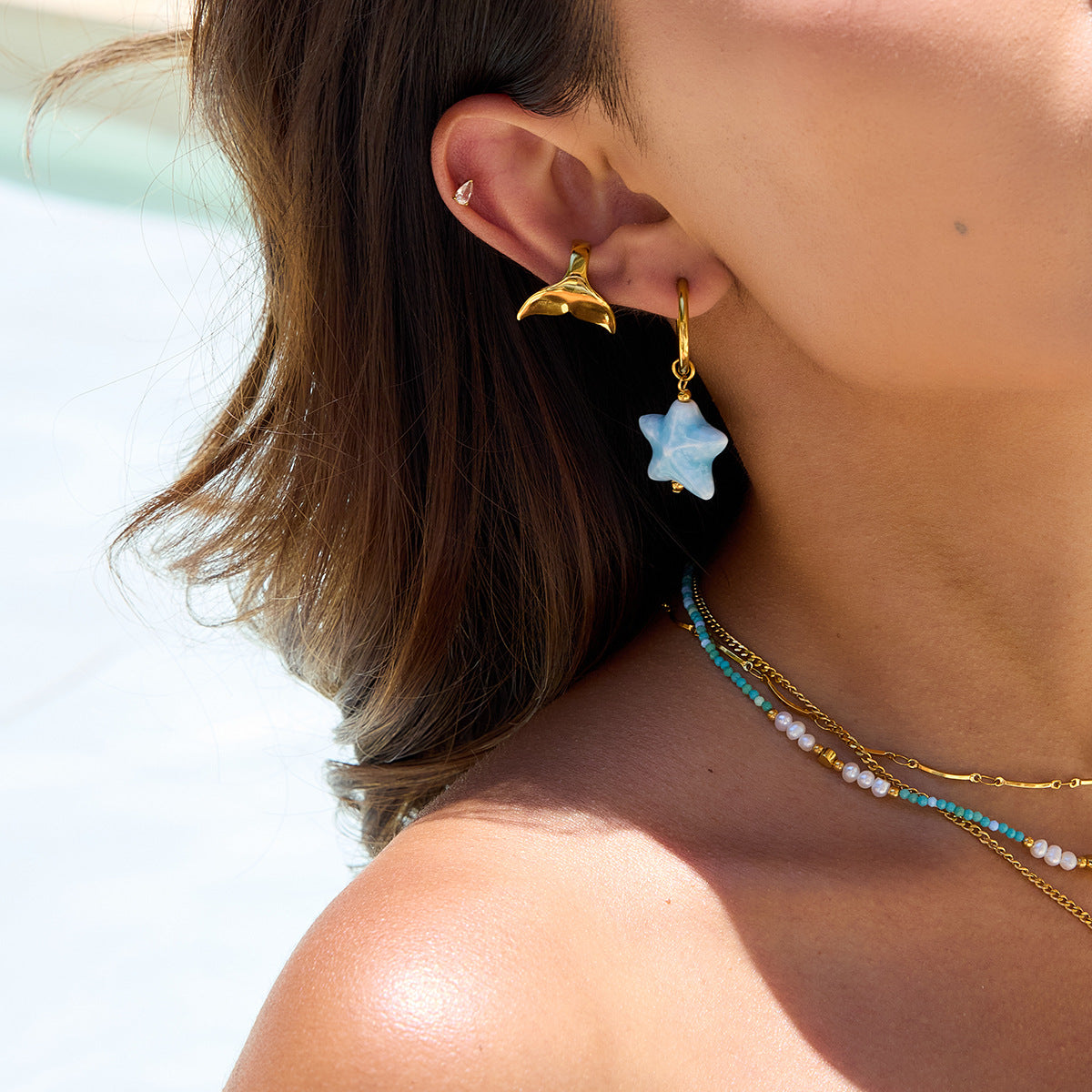 Close-up of a person wearing gold earrings with a star-shaped blue gemstone and a whale-shaped gold earring.