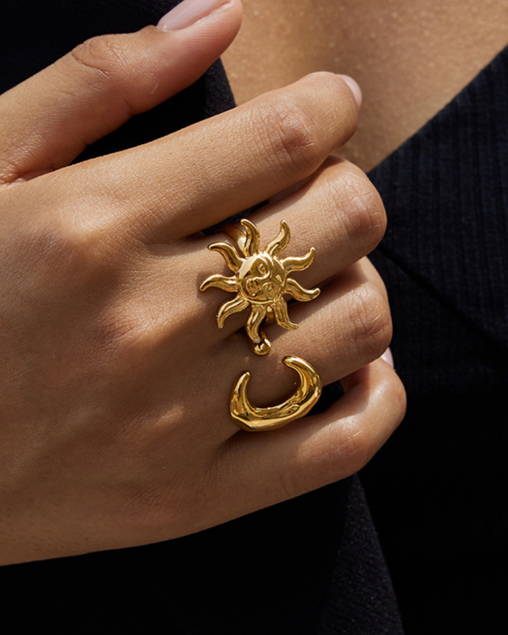 Gold sun and moon ring on a hand against a dark background