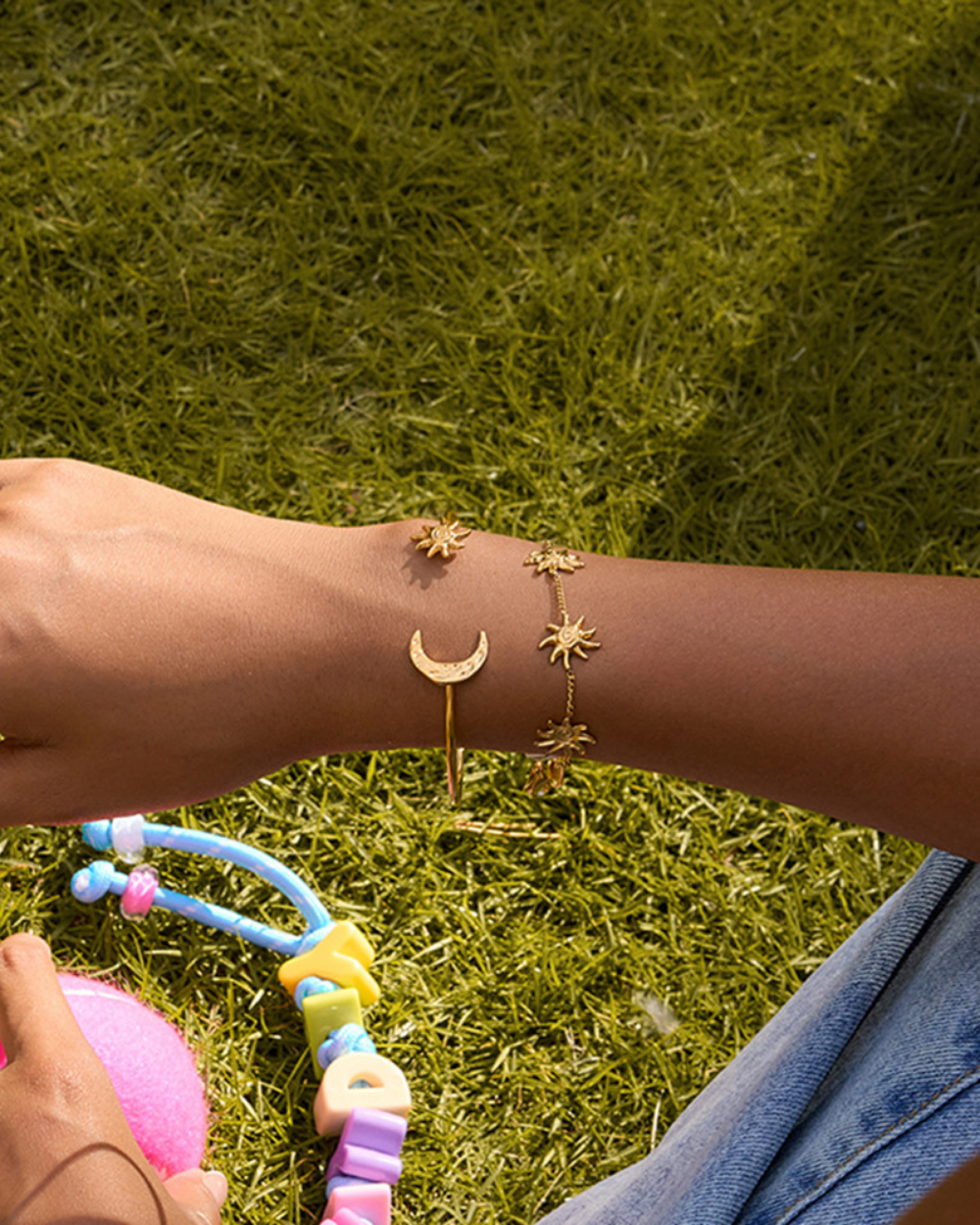 Gold bracelet with celestial design on a person's wrist against a grass background