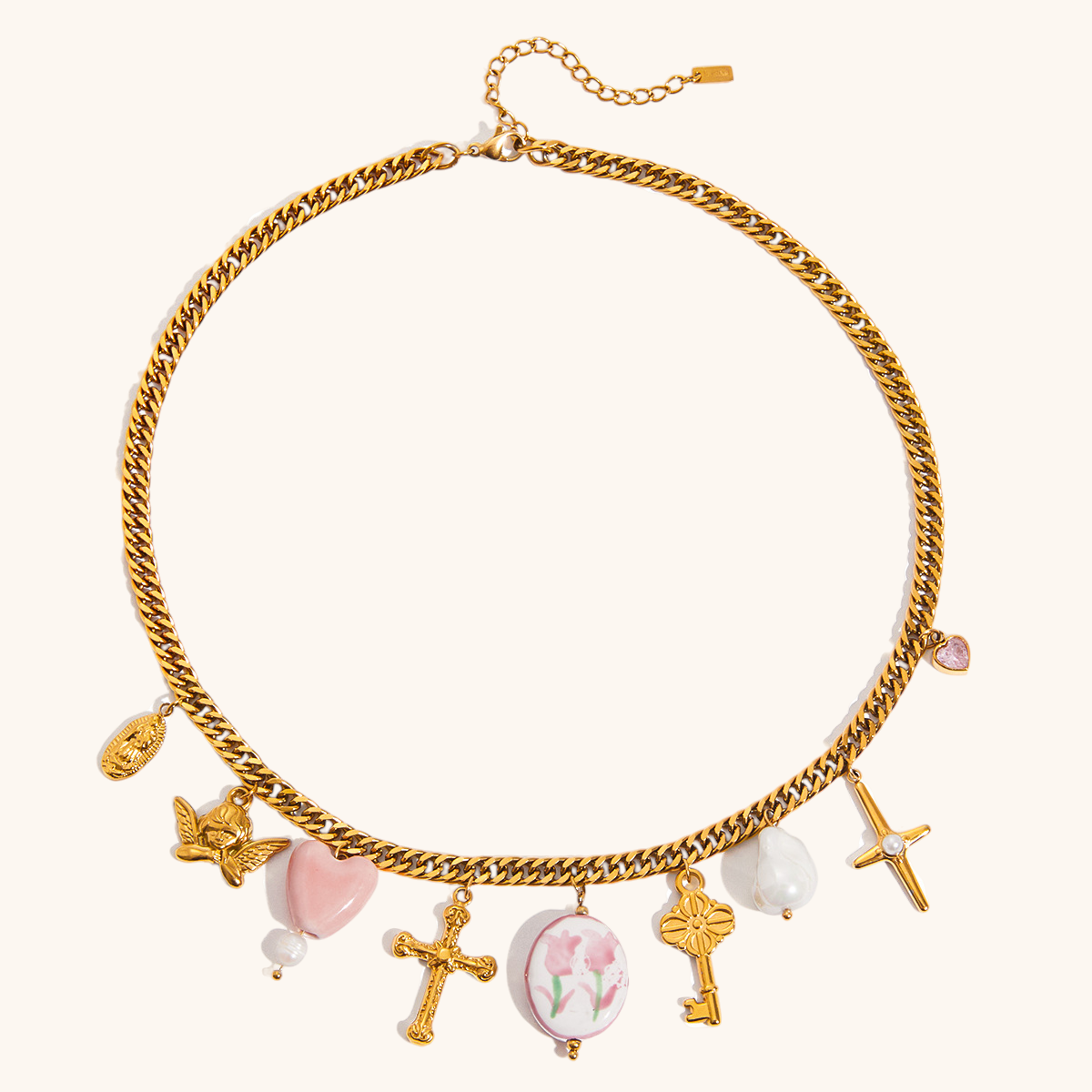 Close-up of gold charm necklace with cross, pearl, and pink heart pendants