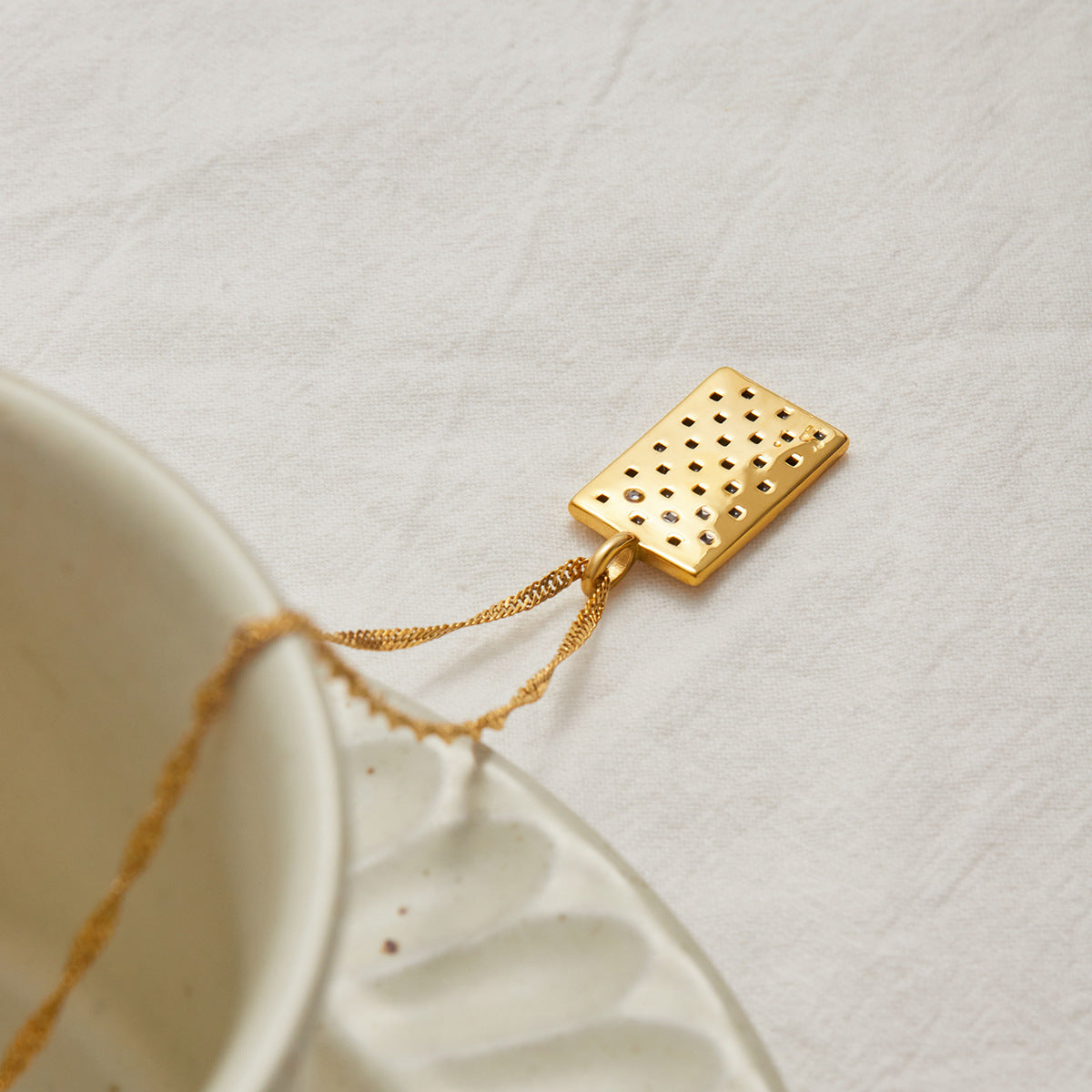 Back view of gold checkered pendant necklace displayed on soft neutral fabric.