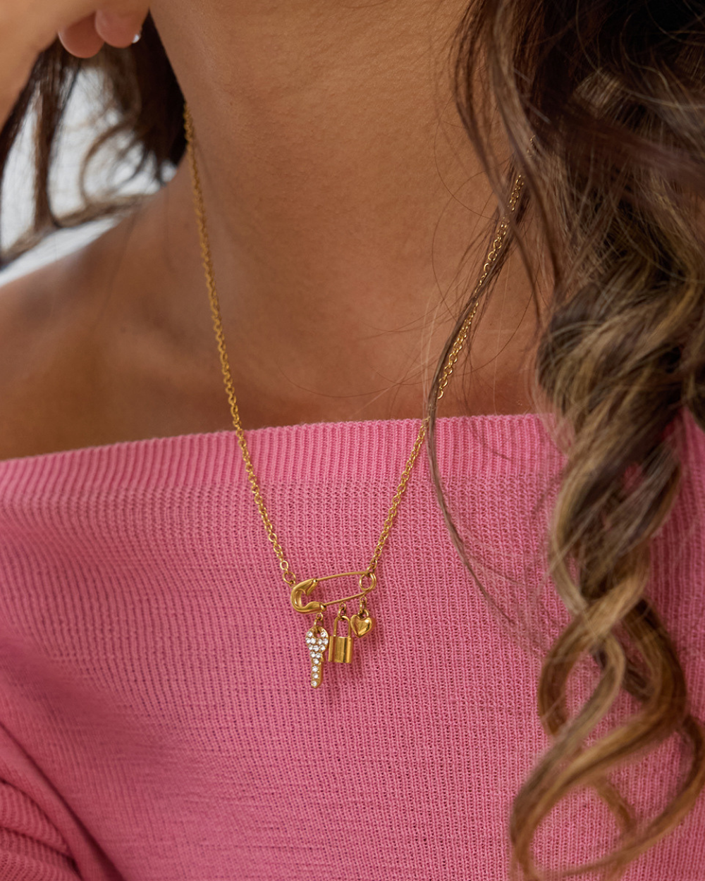 Gold necklace with charms worn by a person against a pink background