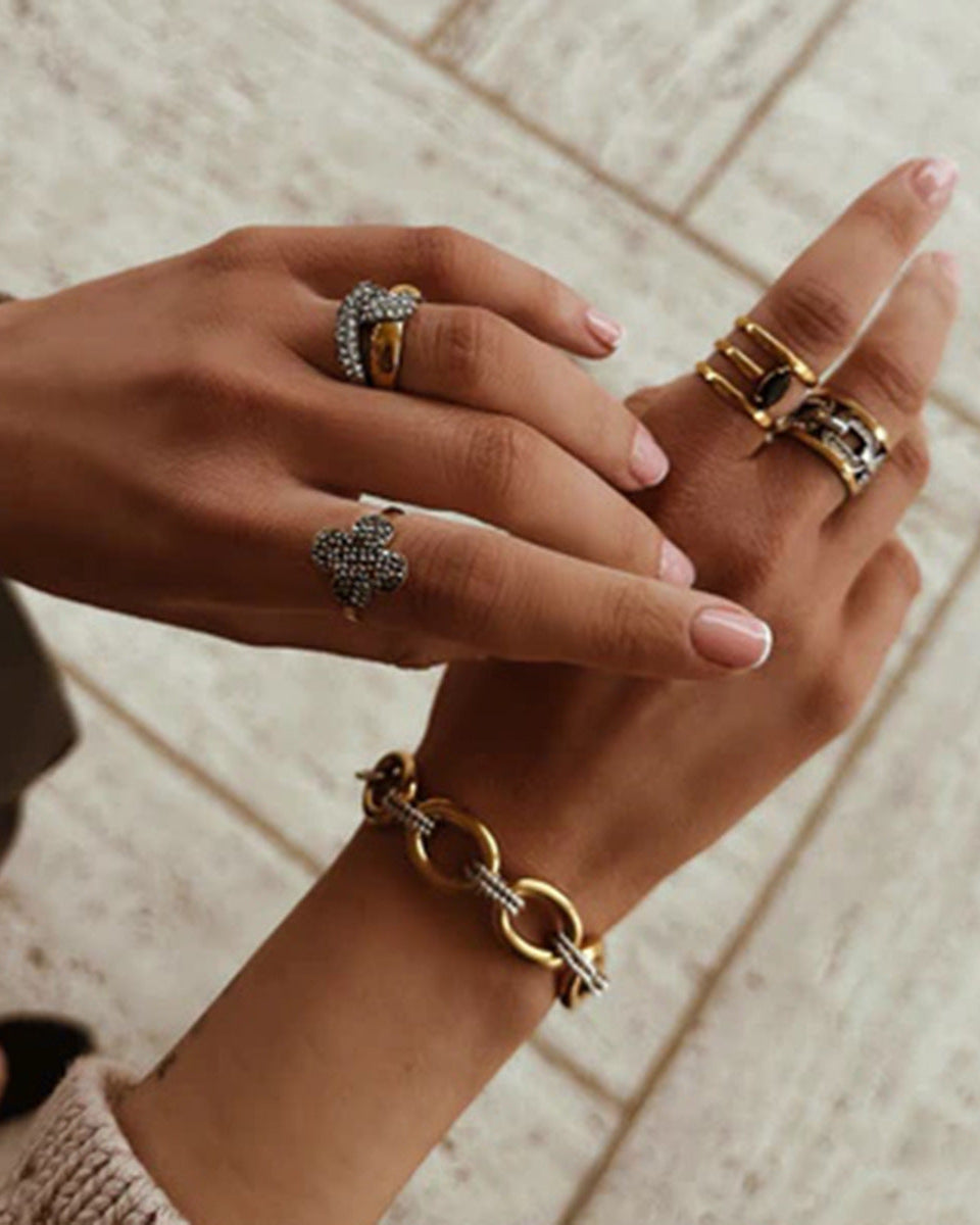 Close-up of a hand wearing multiple gold rings and bracelets on a wooden floor.