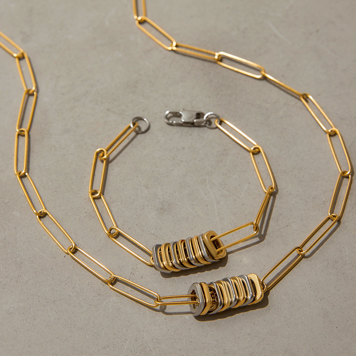 Close-up of chunky gold and silver necklace and bracelet on neutral background, emphasizing bold fashion details.