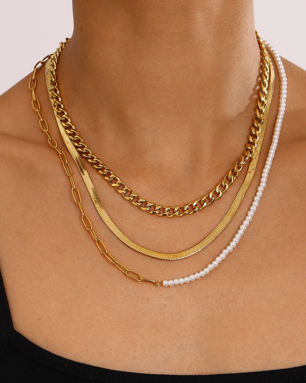 Necklace with gold chain and white pearls on a person's neck against a neutral background