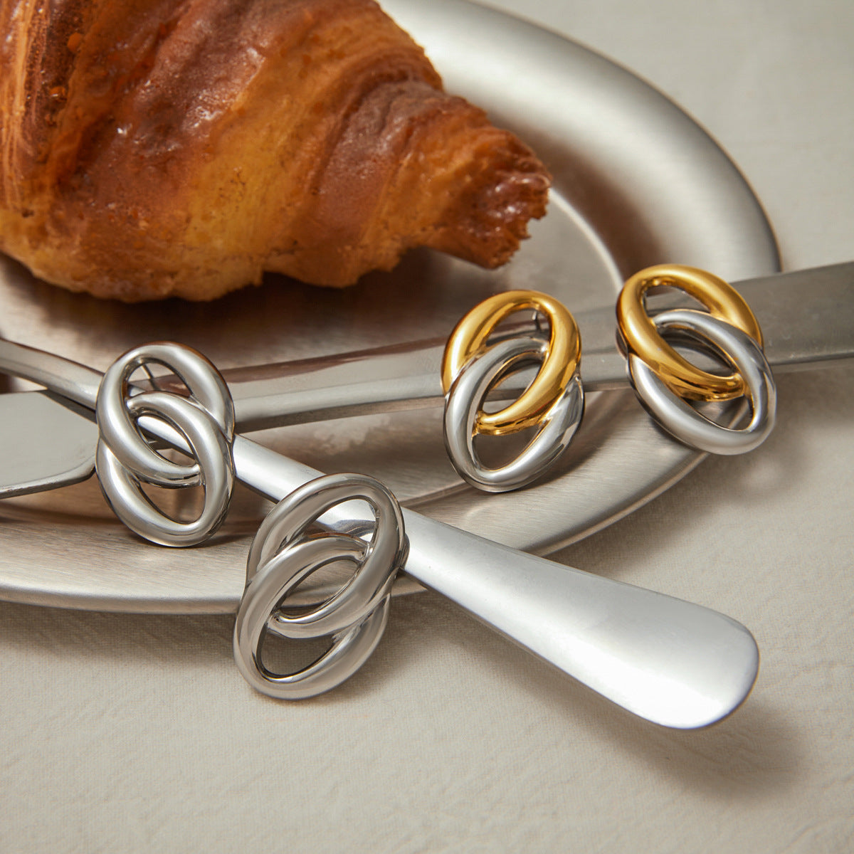 Close-up of mixed metal double hoop earrings in gold and silver finish, shown on silver tray with croissant