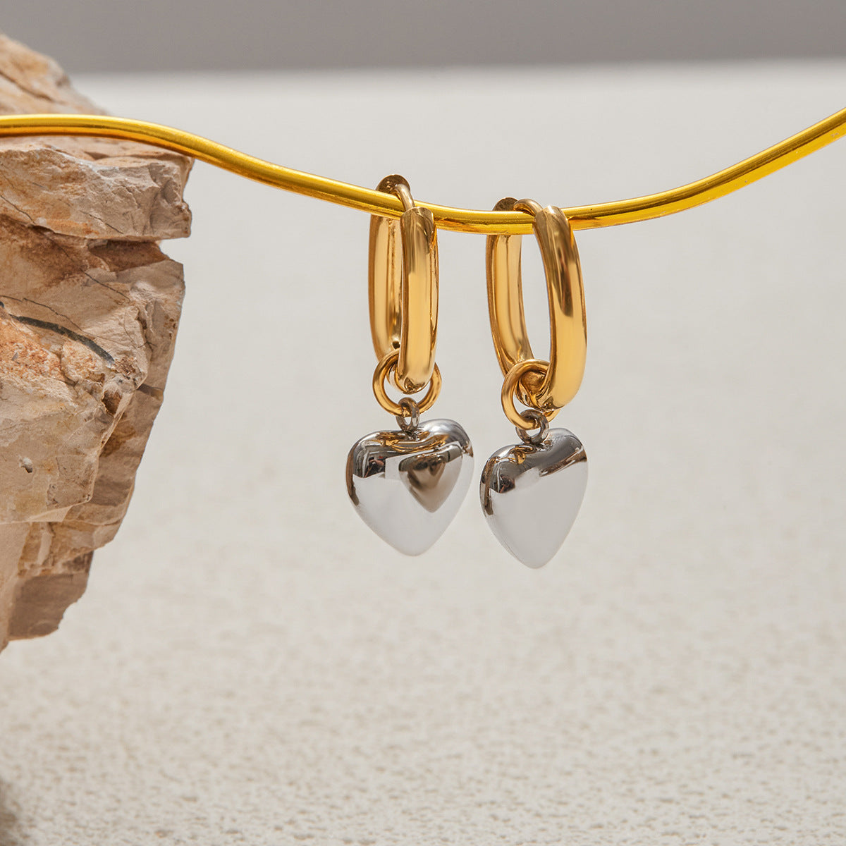 Gold hoop earrings with heart-shaped charms on a neutral background