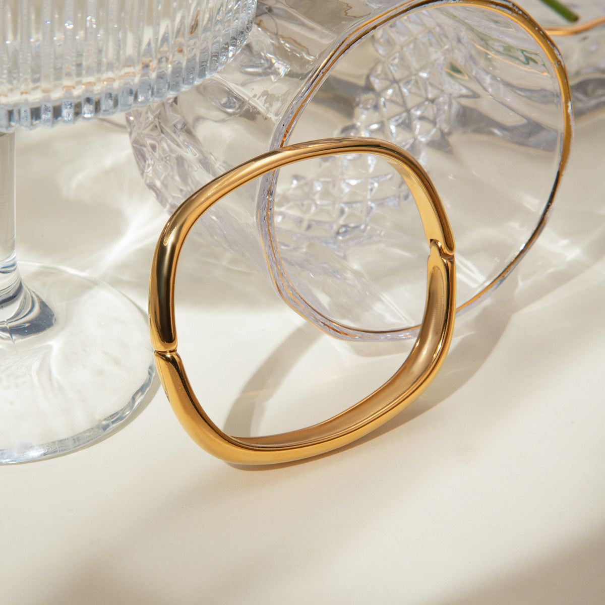 Shiny gold cuff bracelet resting on glassware for aesthetic flatlay