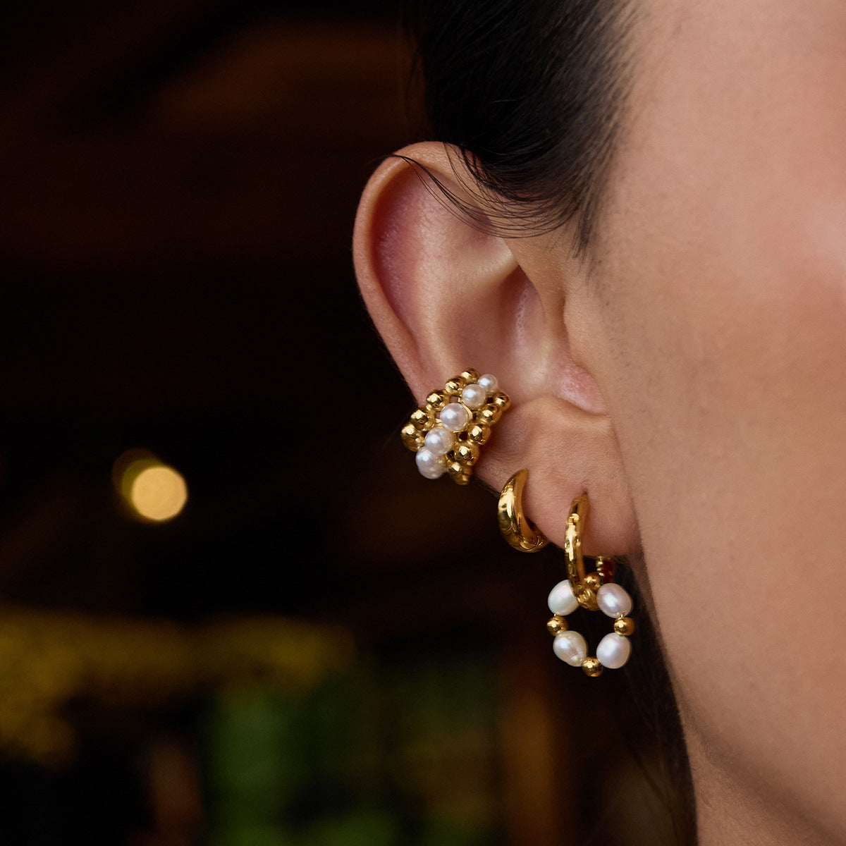 Model wearing layered gold and pearl earrings with non-pierced ear cuff on upper ear