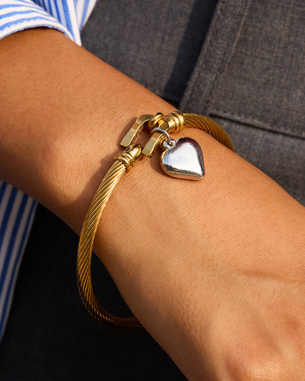 Gold bracelet with a heart charm on a wrist against a dark background
