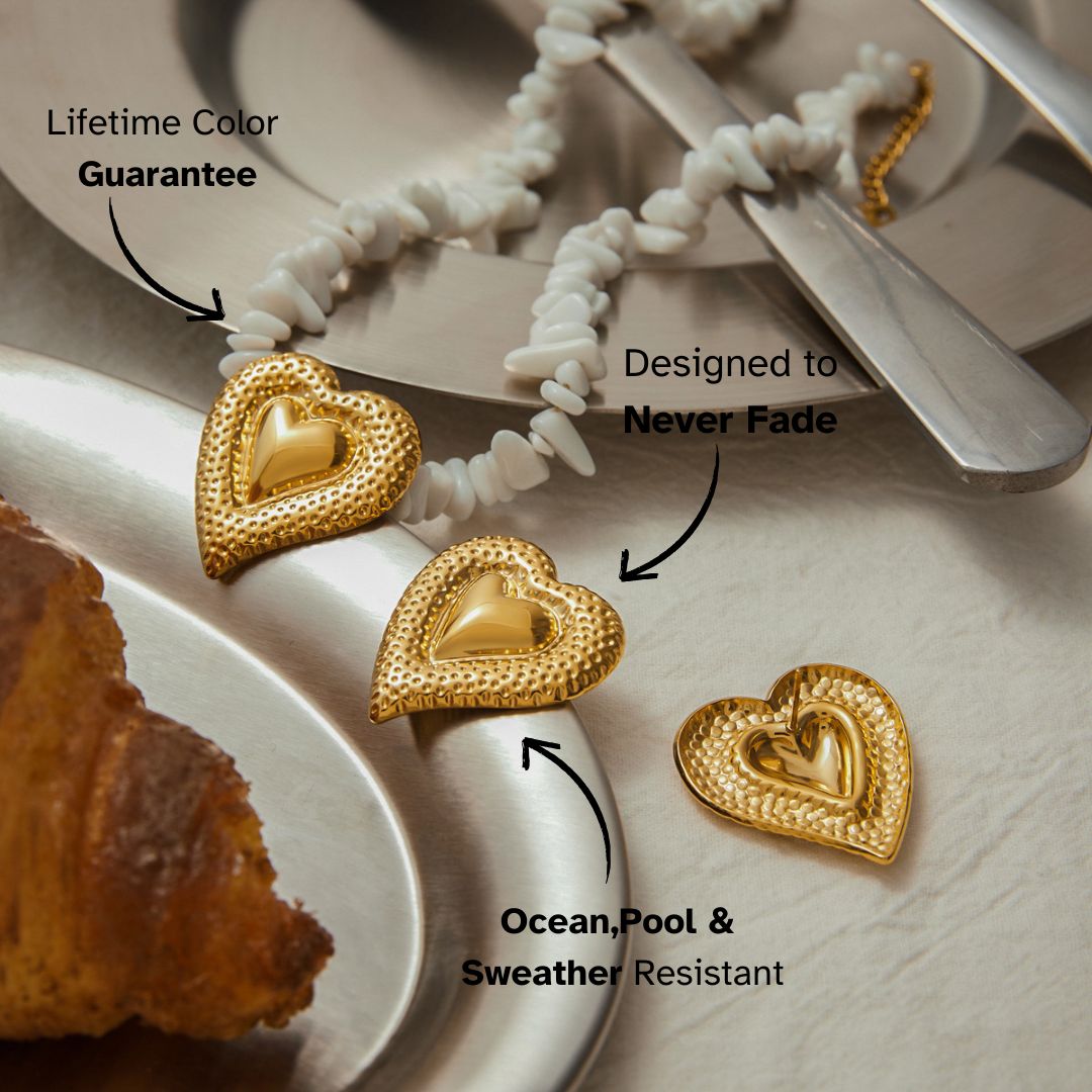 Gold heart earring and matching necklace laid on silver tableware