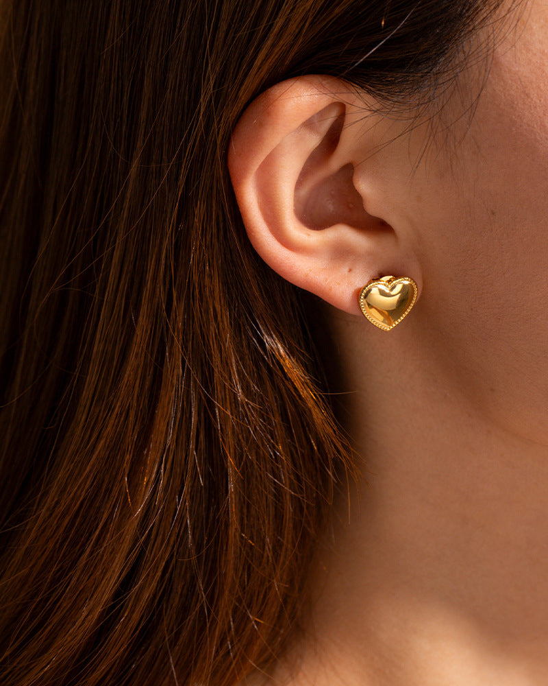 Gold heart-shaped earring worn by a person with brown hair.