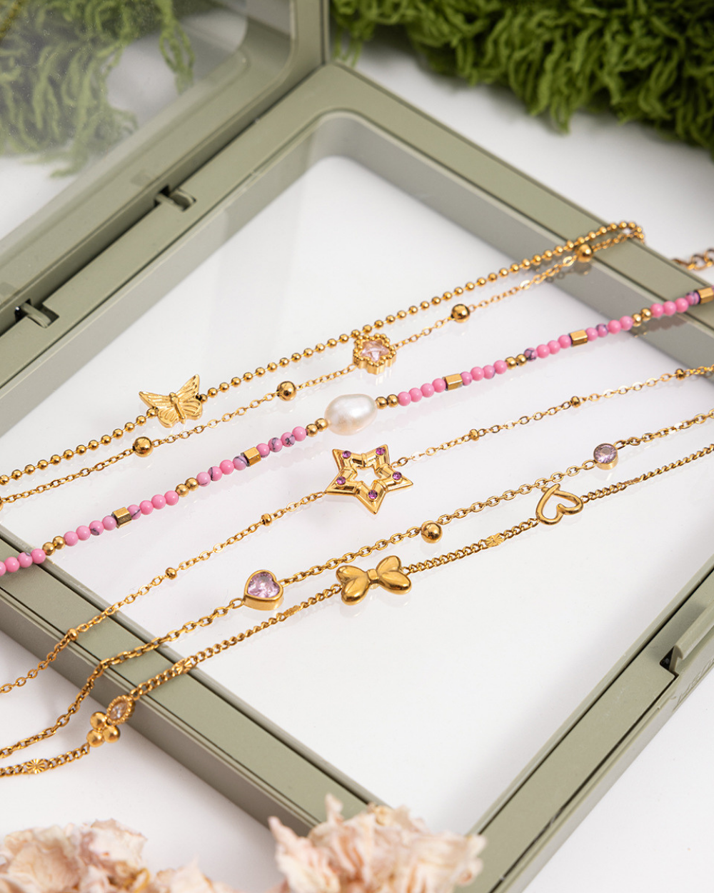 Set of gold and pink beaded necklaces with star, heart, and bow charms in a display case.