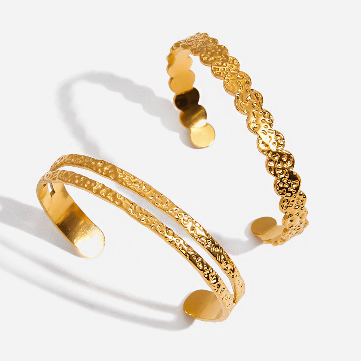 Two gold bangles with textured design on a white background