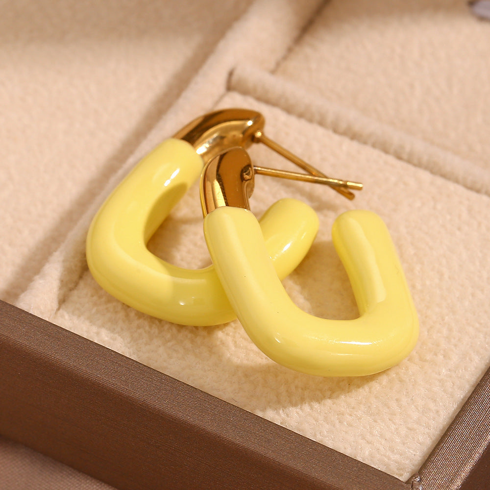 Vibrant yellow U enamel earrings placed inside a neutral-toned jewelry box
