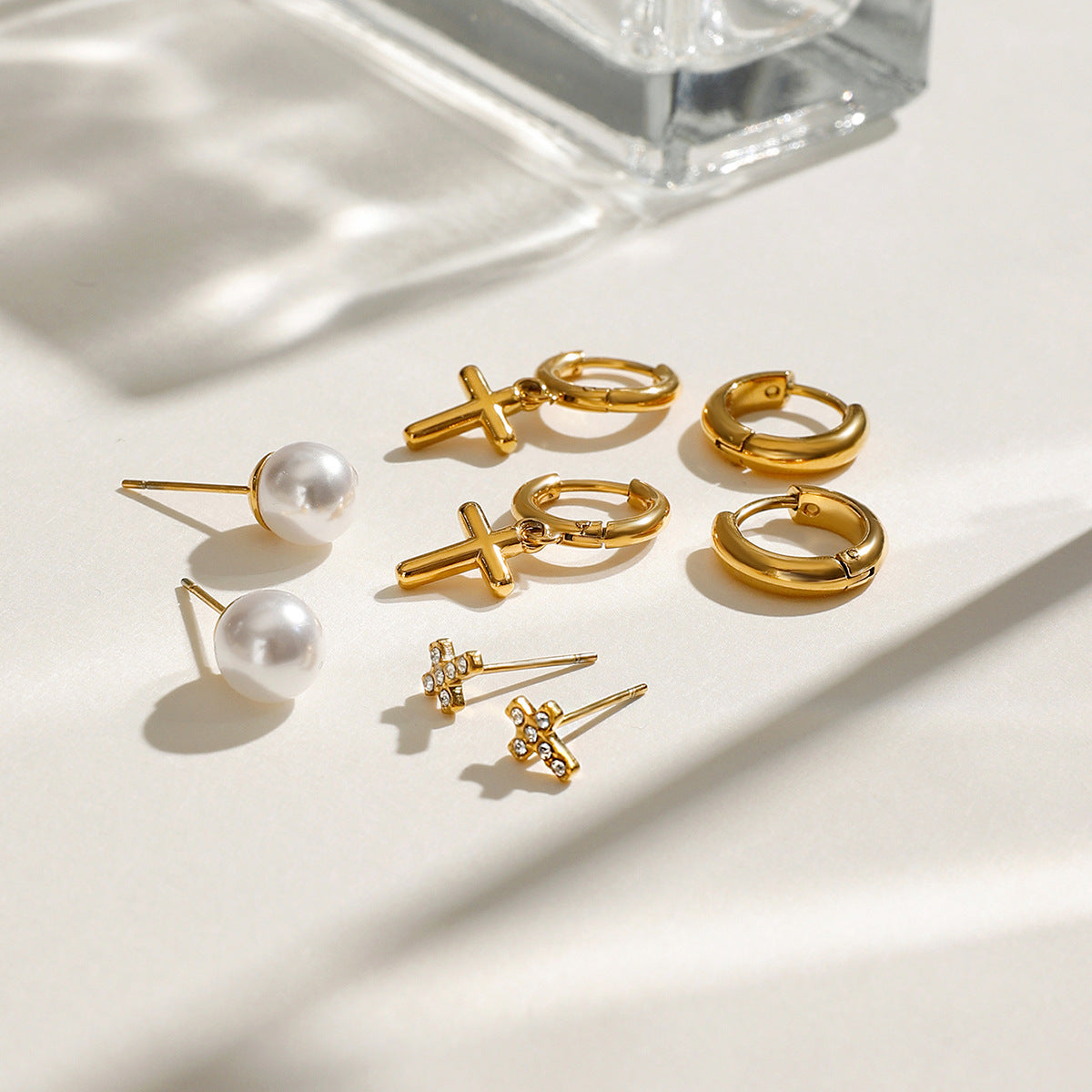Minimalist gold huggie hoops with dangling cross, styled on ear