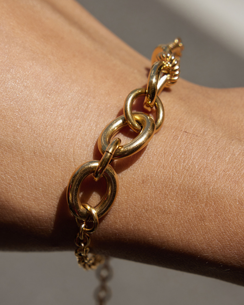 Gold chain bracelet on a wrist with a neutral background