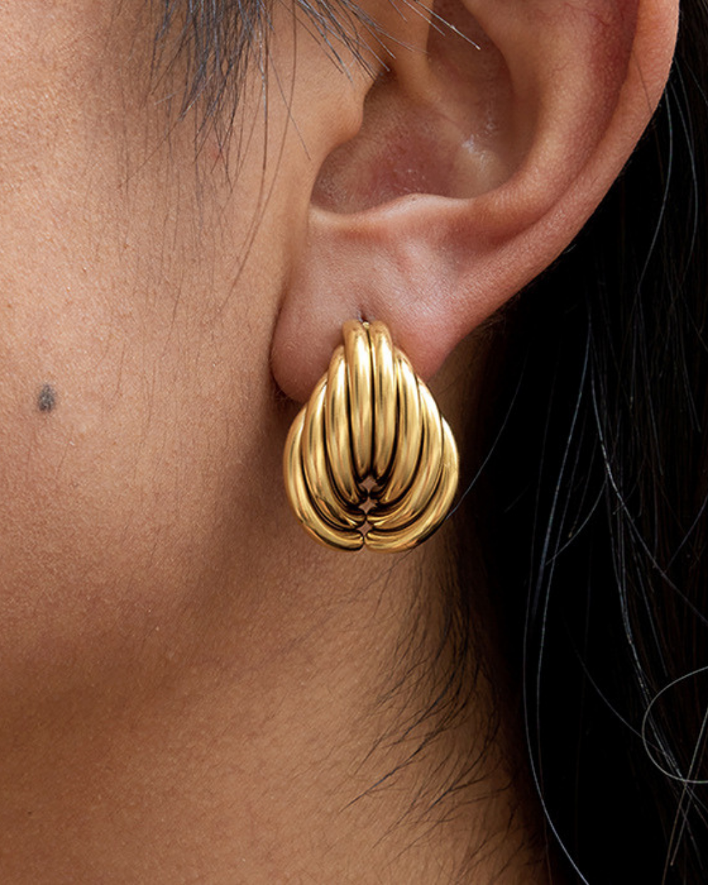 Gold earring worn on an ear with a dark background