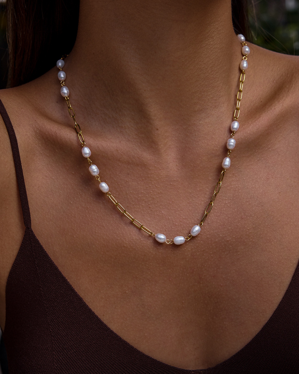 Pearl necklace with gold chain on a person wearing a black top.