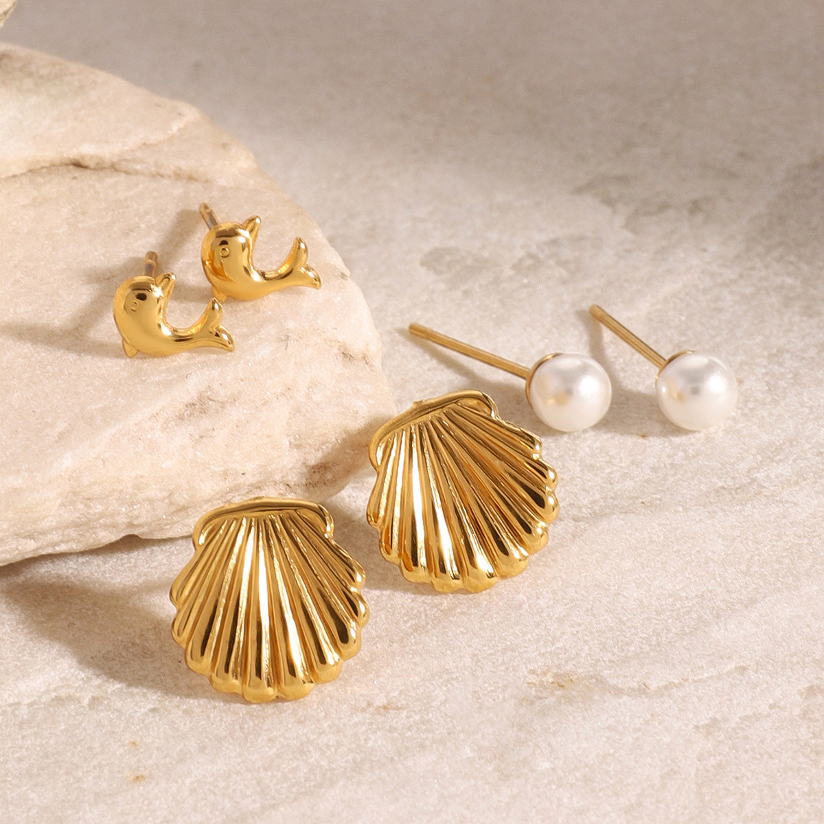 Gold dolphin earrings for women, ocean animal-inspired design on beige surface
