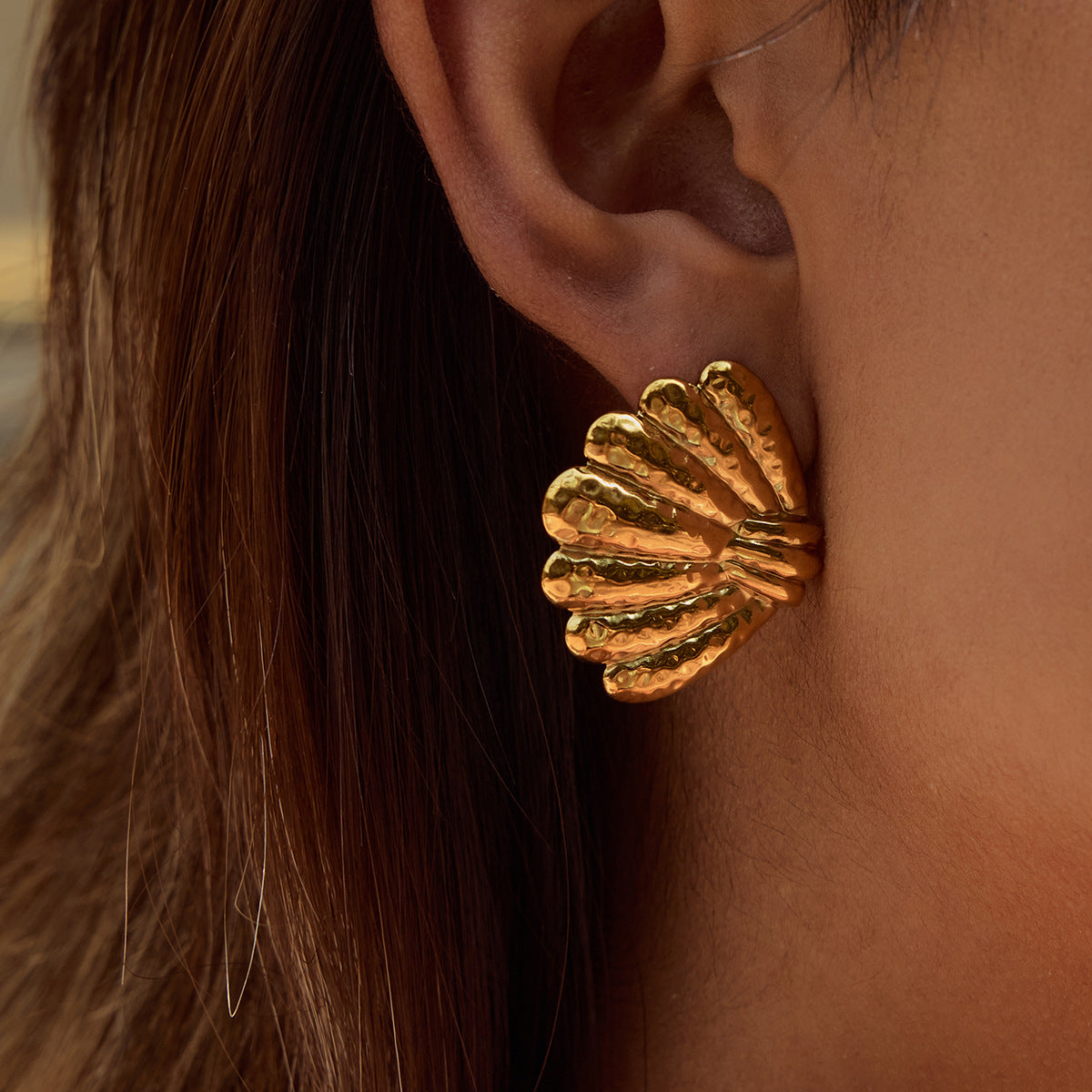 Model showcasing large gold seashell earrings with hair tucked back