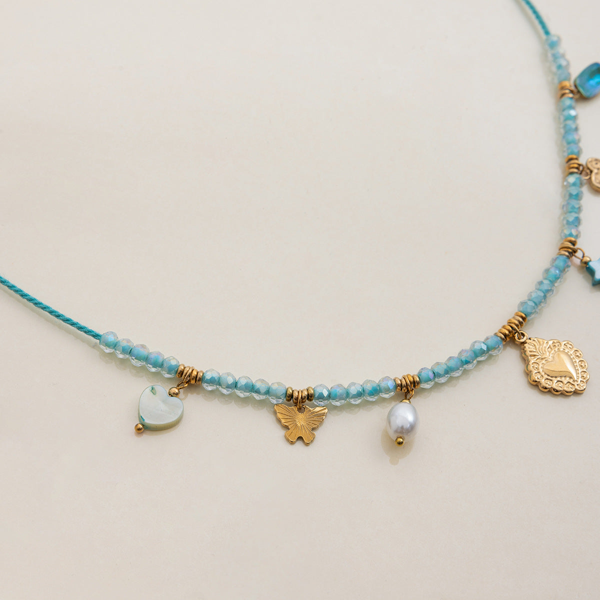 side view of beaded necklace with layered gold charms and blue crystal pendant