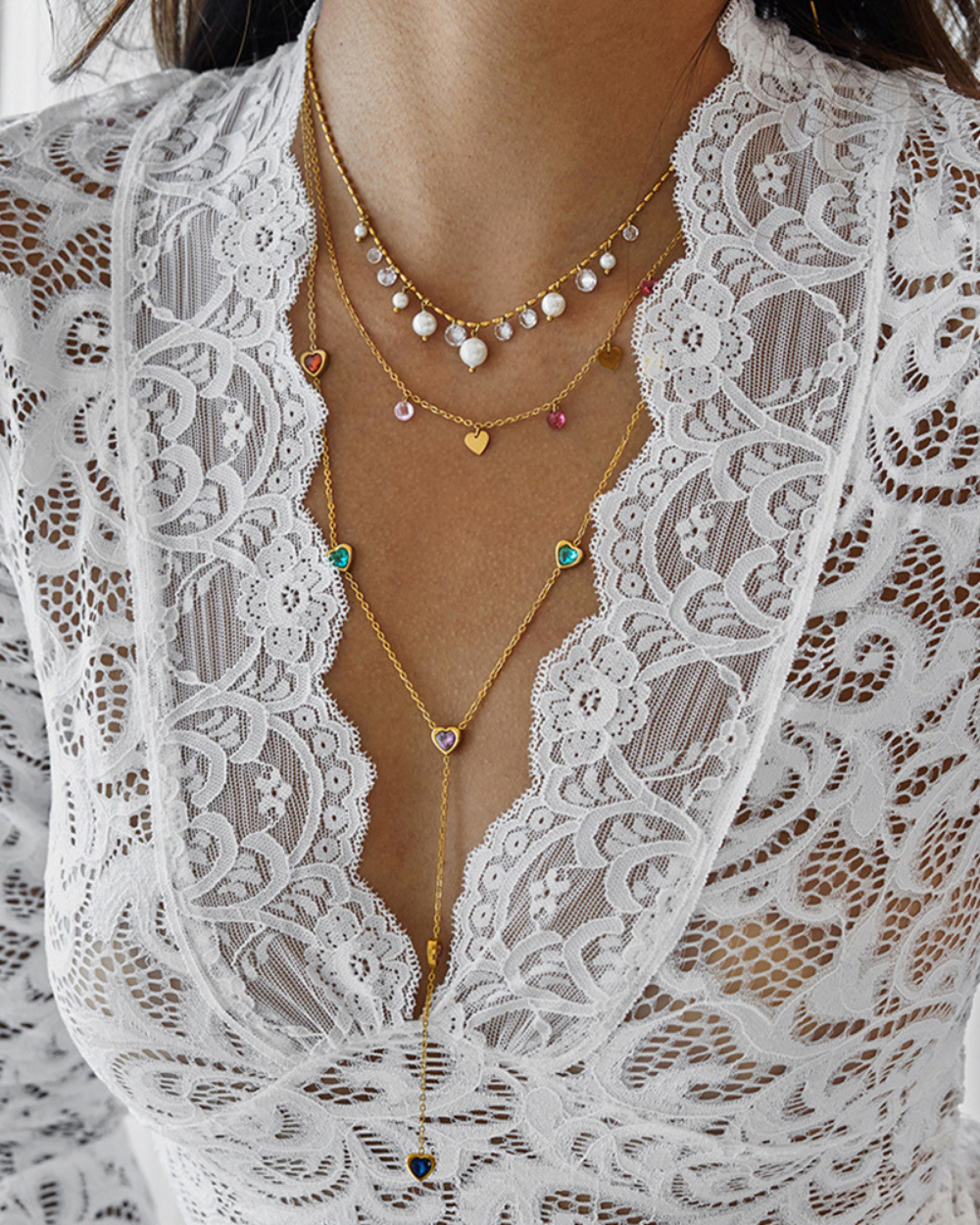 Close-up of a person wearing a white lace garment with layered gold necklaces.