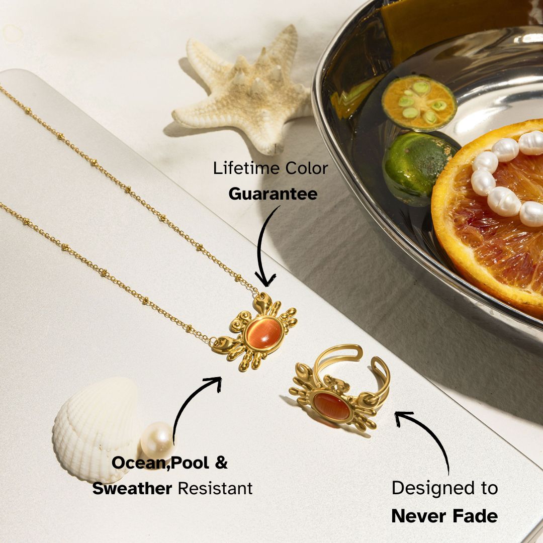 Gold crab motif jewelry set with orange cat-eye stone next to citrus bowl – ocean-themed set for beachside and resort wear