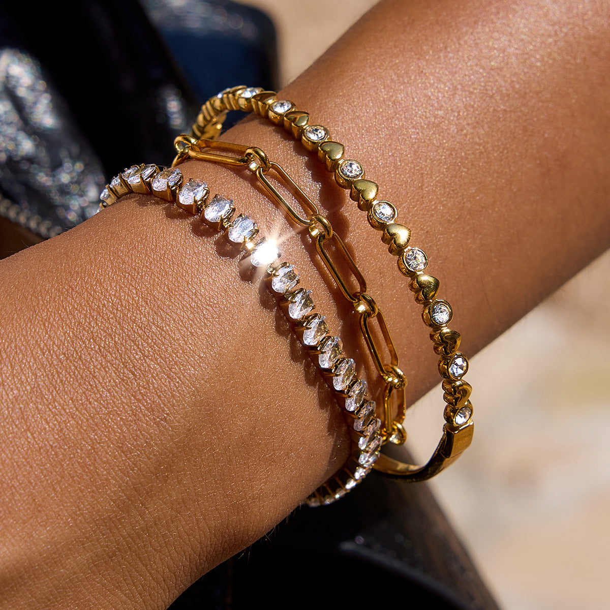 Three gold bracelets with crystals and heart details stacked on female wrist
