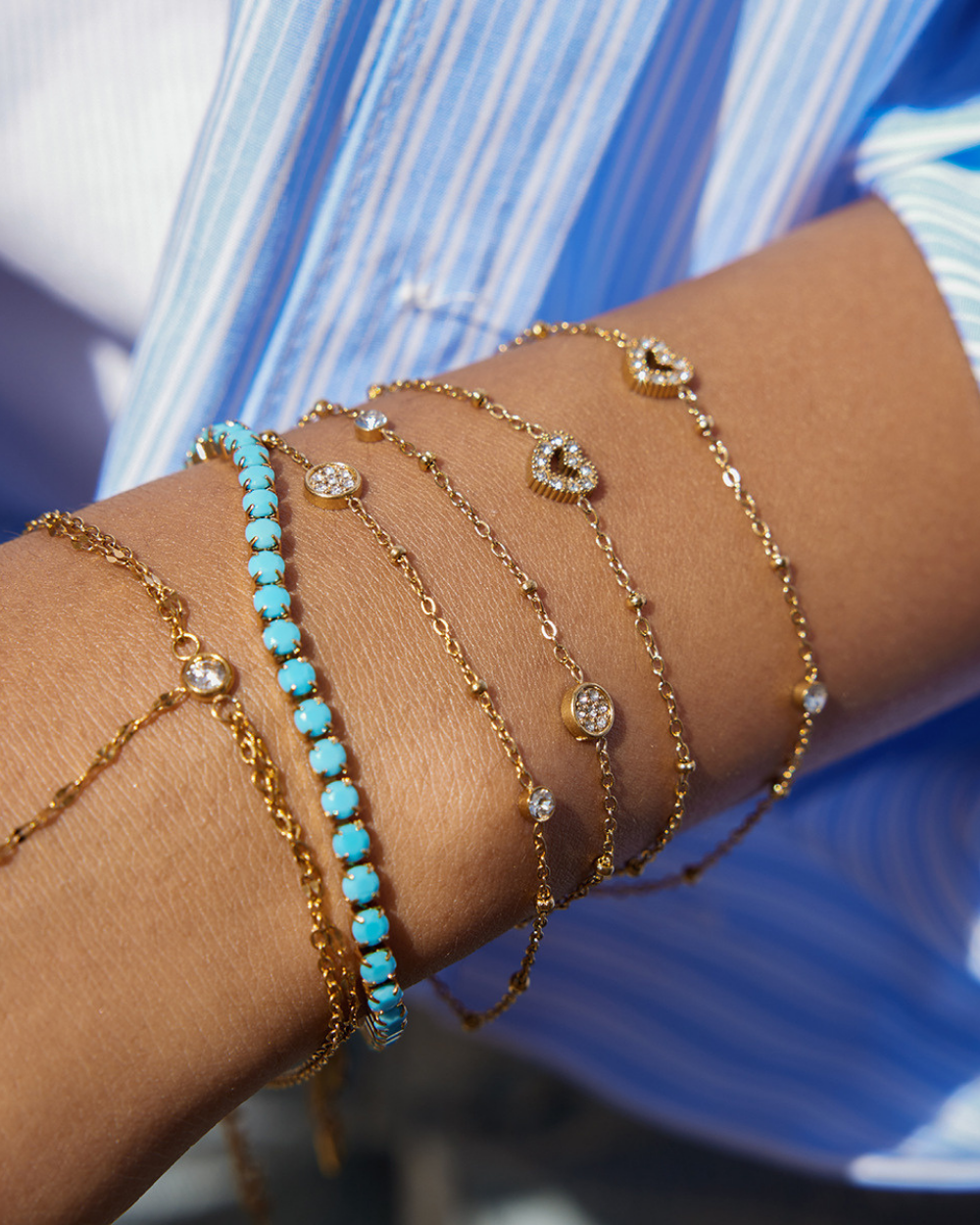 Close-up of a wrist wearing multiple gold and turquoise beaded bracelets against a blurred background.