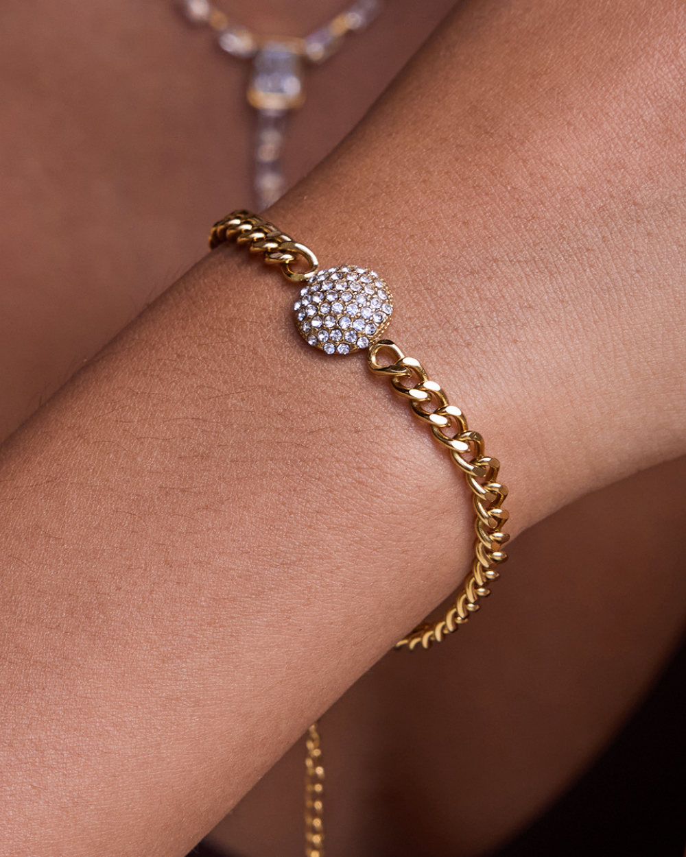 Gold bracelet with a diamond-encrusted clasp on a wrist against a neutral background
