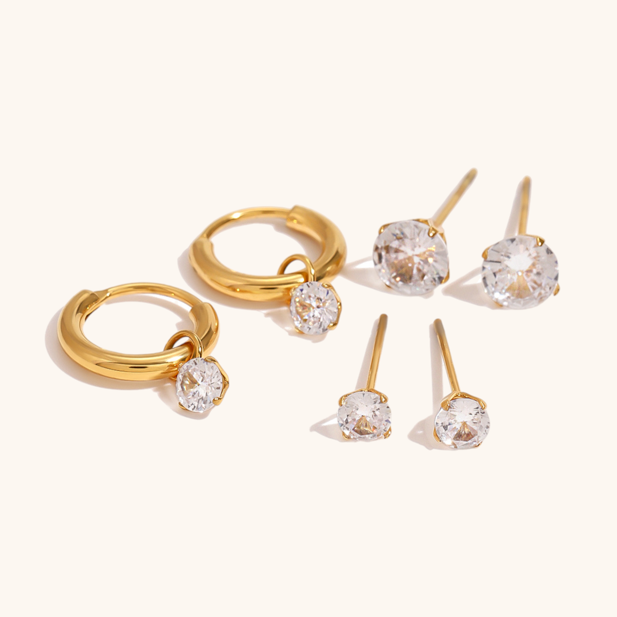 Gold hoop earrings and stud set with sparkling zirconia stones styled on beige background