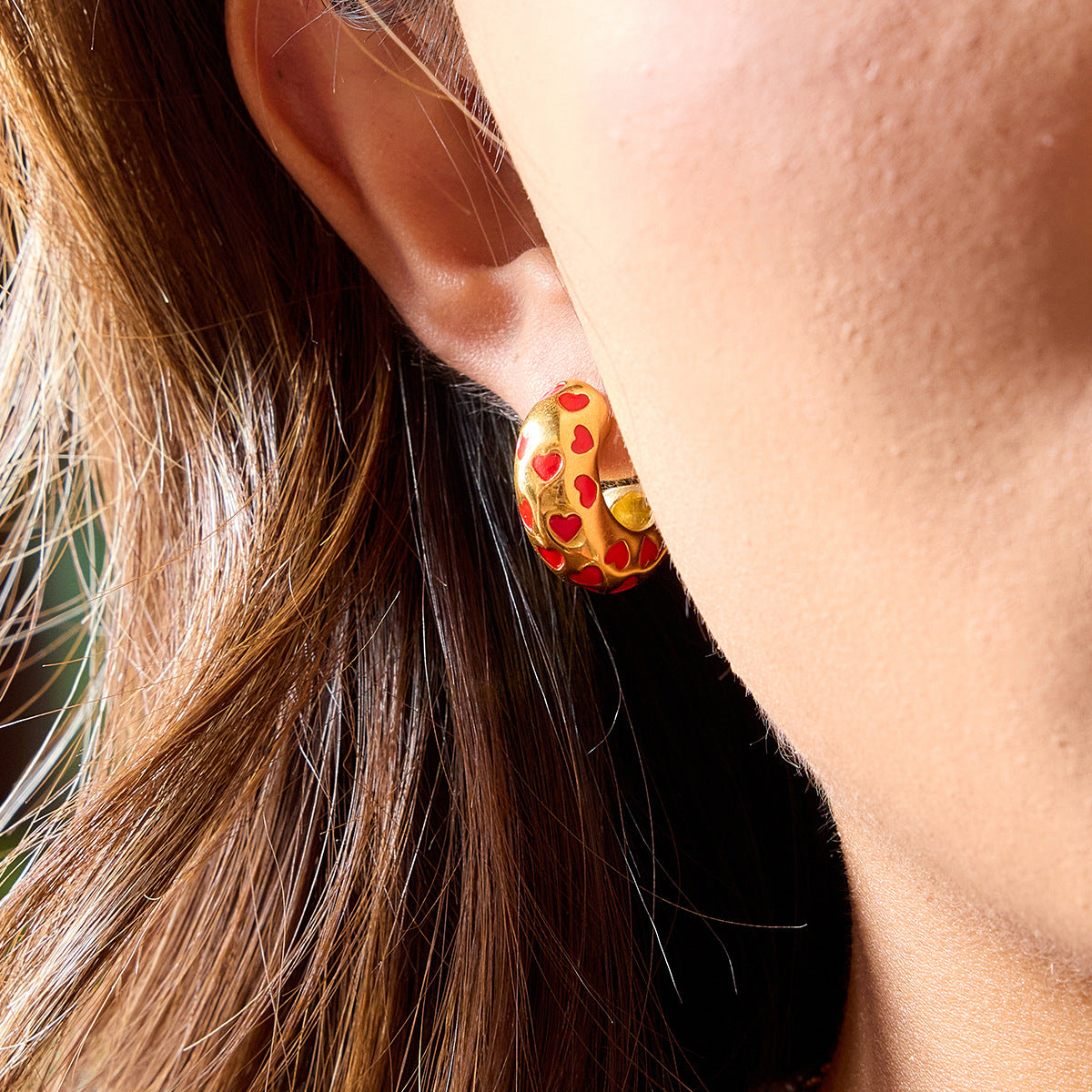 Retro gold earrings with raised red heart details on model’s ear