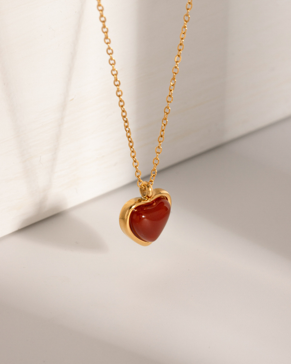 Gold necklace with a heart-shaped red stone pendant on a light background