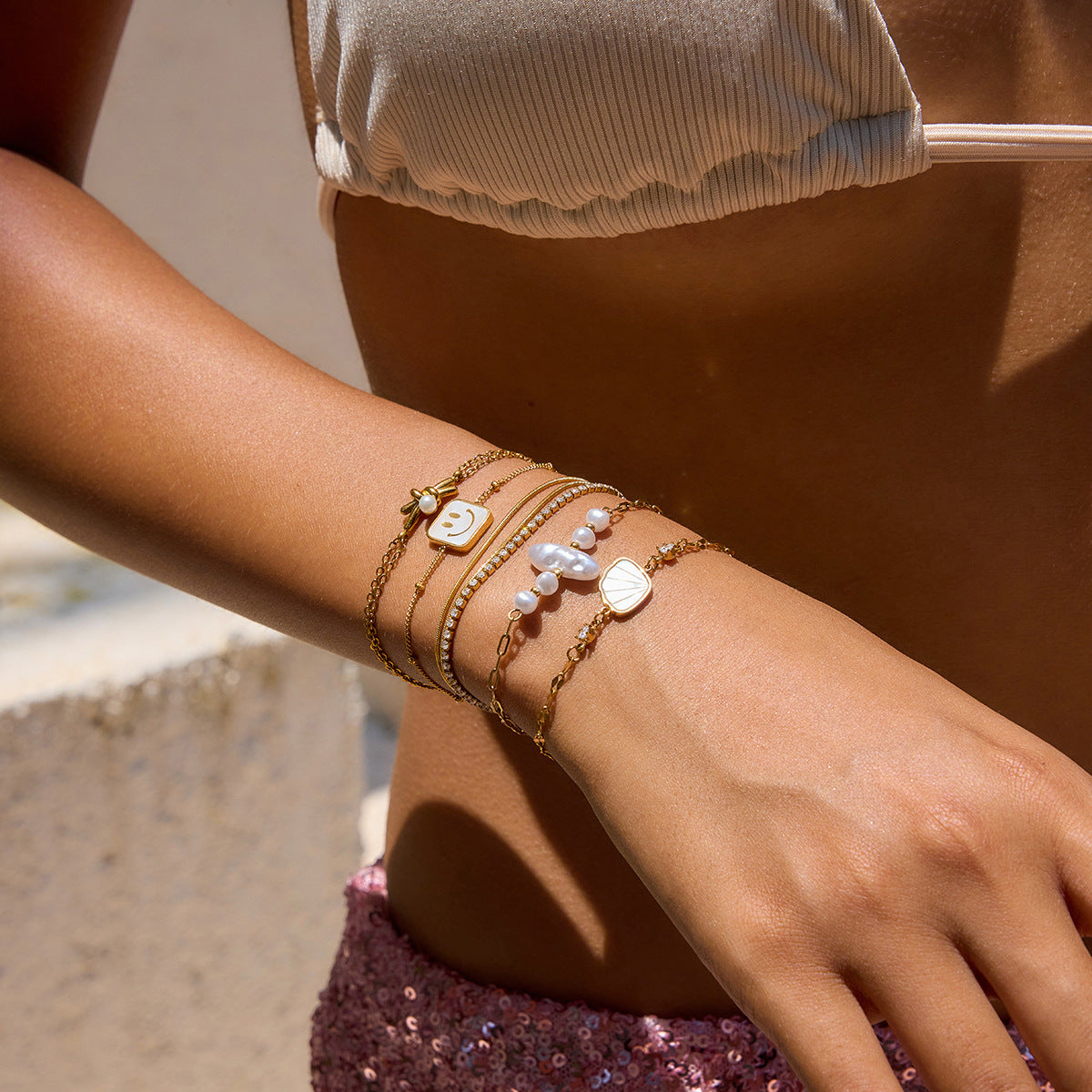 Close-up of a wrist wearing multiple gold and pearl bracelets with a blurred background.