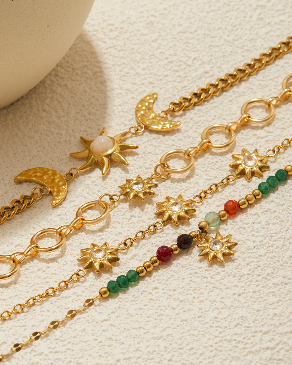 Gold necklaces with sun, moon, and star charms on a textured beige surface