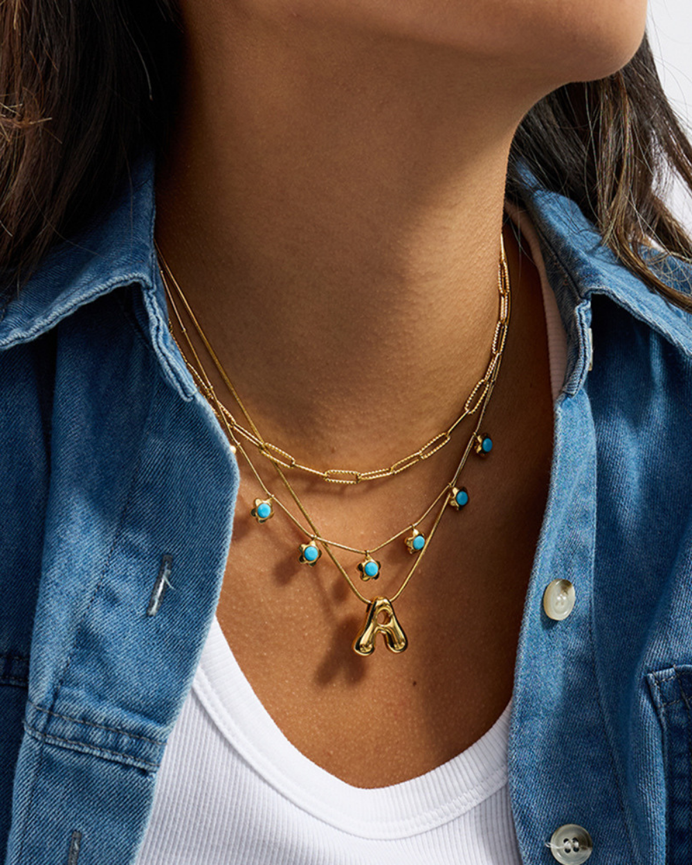 Necklace with gold chain and turquoise beads worn by a person in a denim jacket.