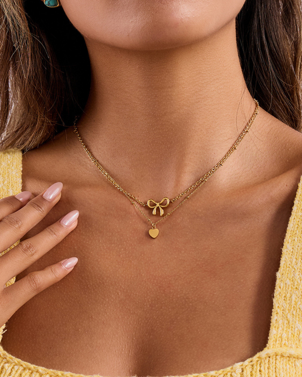 Gold necklace with bow and heart pendant worn by a person in a yellow top.