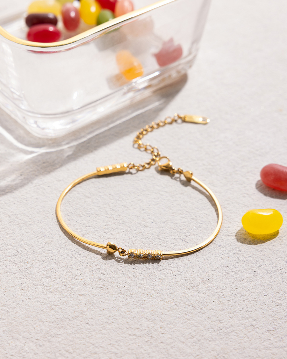 Gold bracelet on a light surface with colorful jelly beans in the background