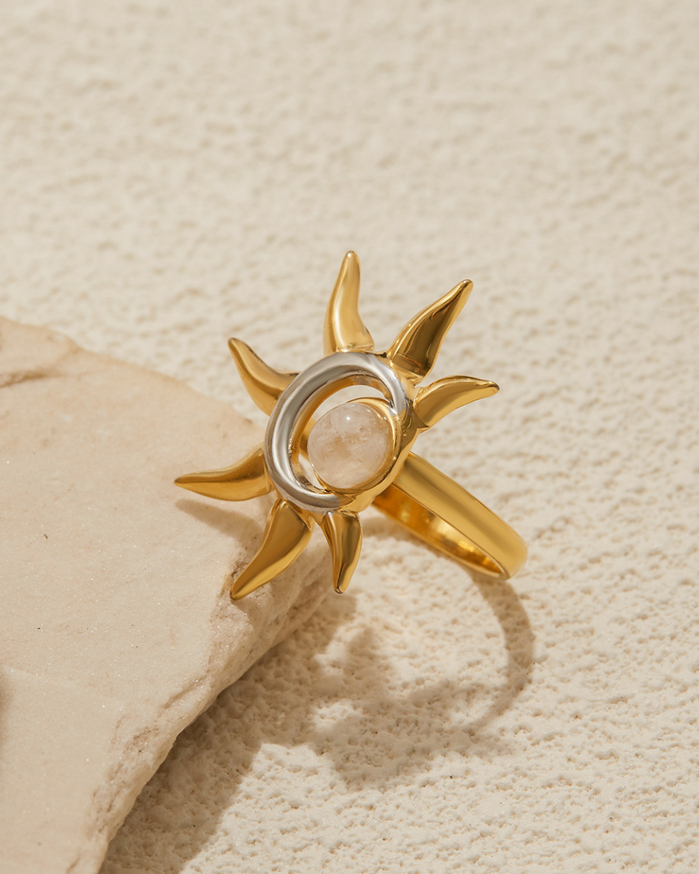Gold ring with sun design on a beige stone background