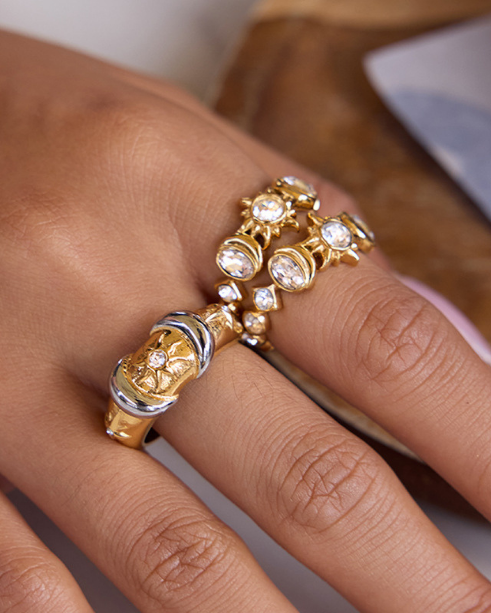Gold ring with gemstones on a finger against a neutral background