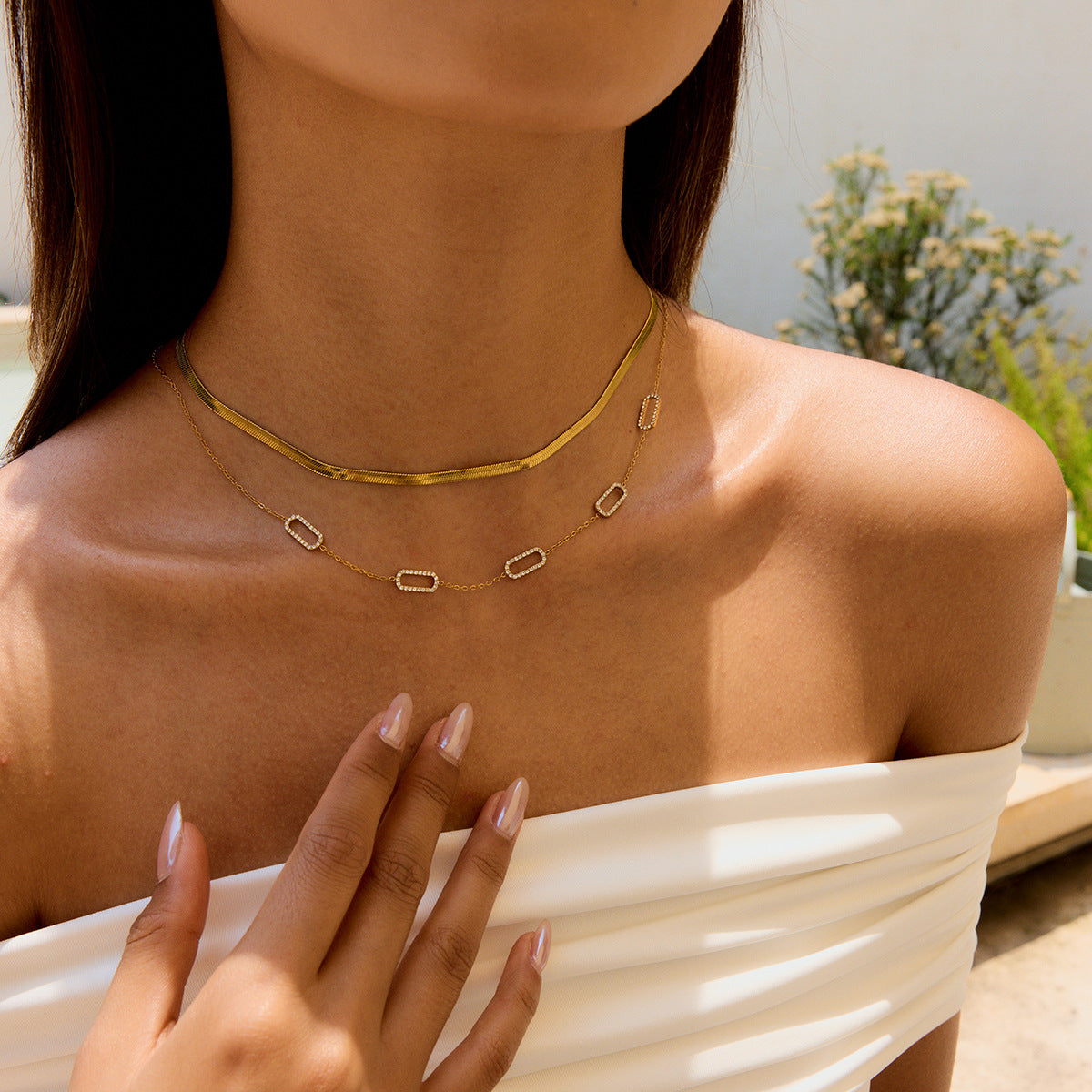 Styled gold necklace with geometric crystal charms worn with off-shoulder white top.
