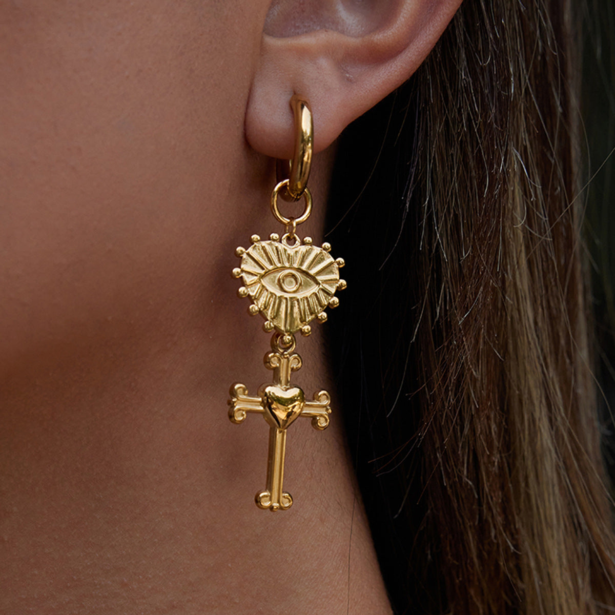 Gold earring with sunburst design and cross detail worn by a person.